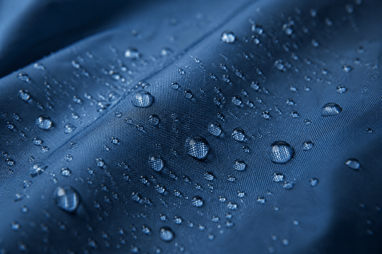 Close-up of waterproof blue fabric with water droplets beading on the surface.